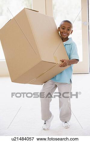 Stock Photo - Young boy holding box in new home smiling. Fotosearch