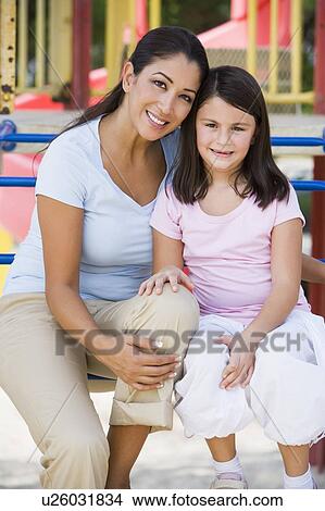 Picture - Mother and daughter girl sitting on playground structure smiling (selective focus). Fotosearch