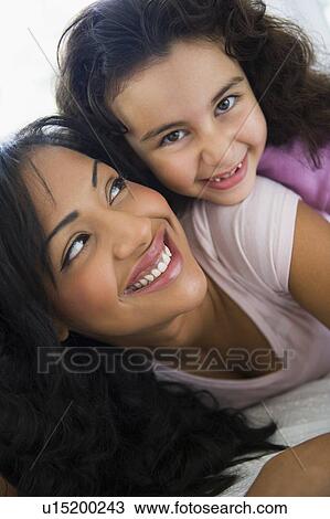 Stock Image - Mother and daughter in living room embracing and smiling (high key/selective focus). Fotosearch