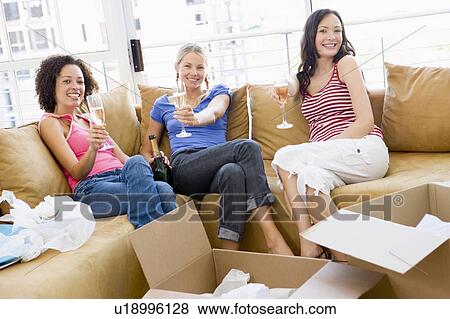 Three girl friends relaxing with champagne by boxes in new home smiling View Large Photo Image Stock Photo - Three girl friends relaxing with champagne by boxes in new home smiling. Fotosearch