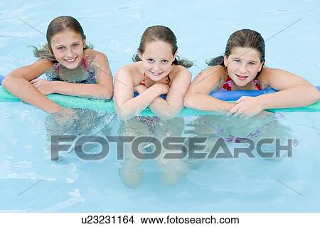 Picture - Three young girl friends in swimming pool with pool noodle smiling. Fotosearch