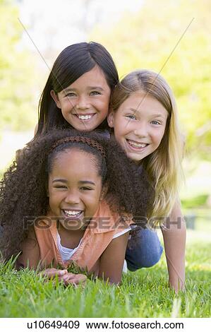 Three young girl friends piled up on top of each other outdoors smiling View Large Photo Image Stock Photo - Three young girl friends piled up on top of each other outdoors smiling. Fotosearch