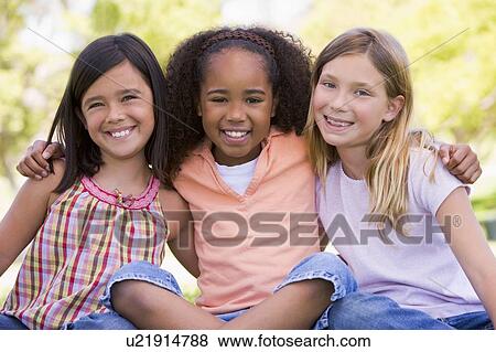 Stock Photo - Three young girl friends sitting outdoors smiling. Fotosearch