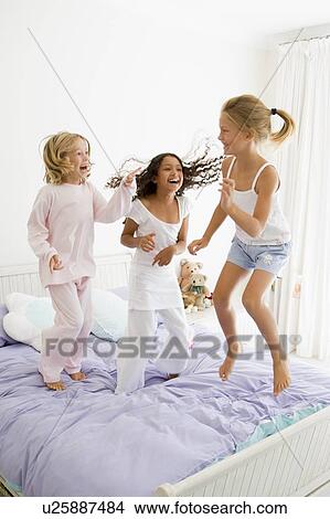 Picture - Three Young Girls Jumping On A Bed In Their Pajamas. Fotosearch