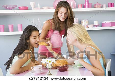 Picture - Three young woman sitting at a table having tea and a snack. Fotosearch
