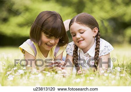 Stock Image - Two sisters lying outdoors with flower smiling. Fotosearch