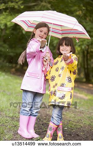 Stock Photo - Two sisters outdoors in rain with umbrella smiling. Fotosearch