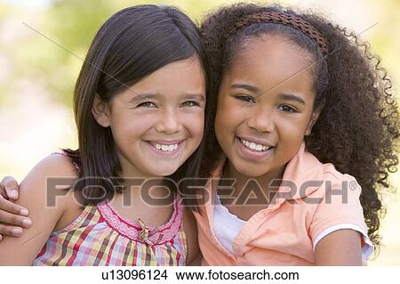 Picture - Two young girl friends sitting outdoors smiling. Fotosearch