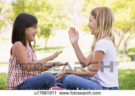 Stock Image - Two young girl friends sitting outdoors playing patty cake smiling. Fotosearch