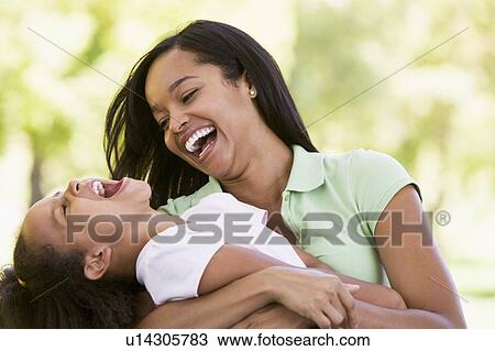 Stock Image - Woman and young girl outdoors embracing and laughing. Fotosearch