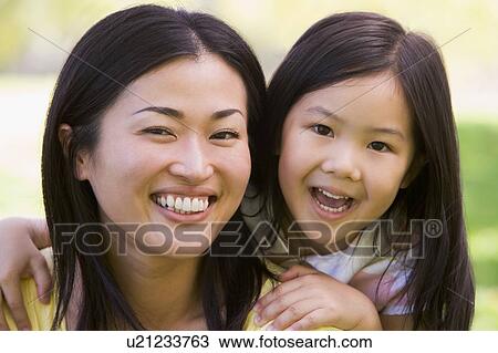 Stock Image - Woman and young girl outdoors embracing and smiling. Fotosearch