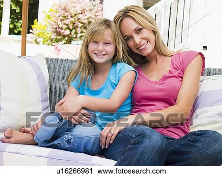 Stock Image - Woman and young girl sitting on patio smiling. Fotosearch