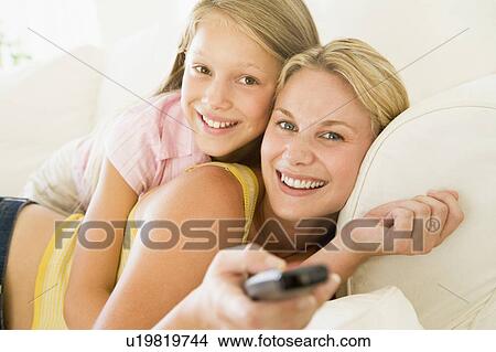 Woman and young girl with remote control embracing on sofa smiling View Large Photo Image Picture - Woman and young girl with remote control embracing on sofa smiling. Fotosearch
