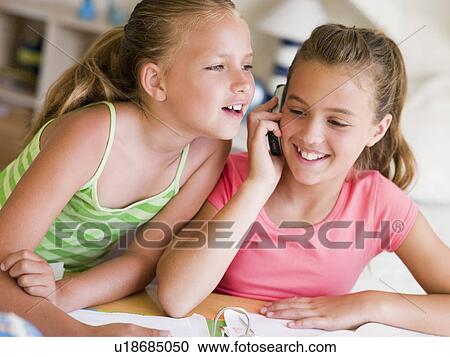 Stock Image - Young Girls Distracted From Their Homework, Talking On A Cellphone. Fotosearch