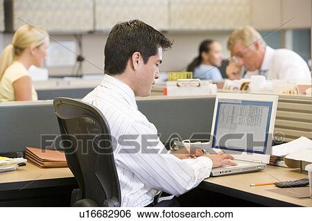 Stock Photograph - Businessman in cubicle using laptop. Fotosearch