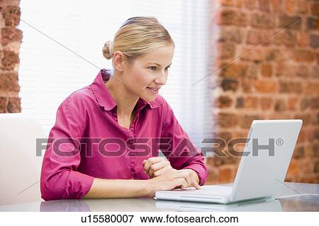 Stock Photo - Businesswoman sitting in office using laptop smiling. Fotosearch