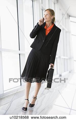 Stock Photo - Businesswoman walking in corridor talking on cellular phone. Fotosearch