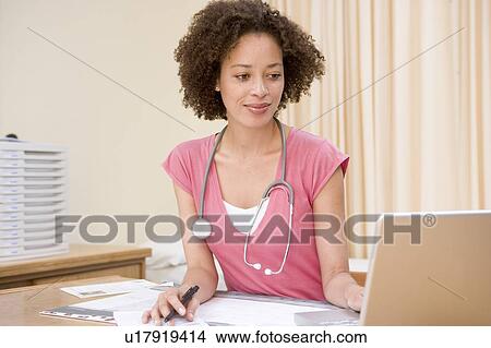 Doctor using laptop in doctor's office smiling View Large Photo Image Picture - Doctor using laptop in doctor's office smiling. Fotosearch
