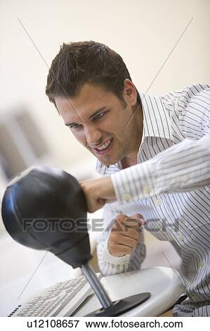 Stock Photo - Man sitting in computer room using small punching bag for stress relief. Fotosearch