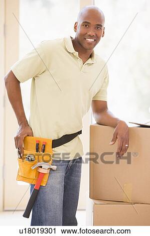 Man wearing tool belt standing by boxes in new home smiling View Large Photo Image Stock Image - Man wearing tool belt standing by boxes in new home smiling. Fotosearch