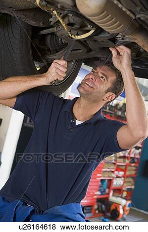 Stock Photo - Mechanic working under car smiling. Fotosearch