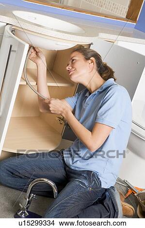 Picture - Plumber working on sink smiling. Fotosearch