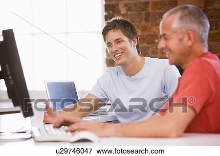Stock Photo - Two businessmen in office typing on computer and smiling. Fotosearch