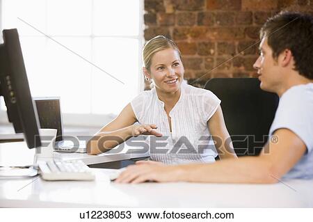 Stock Image - Two businesspeople in office talking and smiling. Fotosearch
