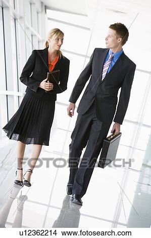 Picture - Two businesspeople walking in corridor talking. Fotosearch