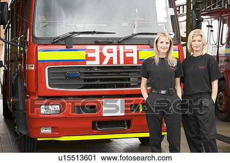 Stock Image - Two firefighters standing in front of fire engine. Fotosearch
