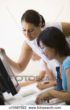 Stock Image - Two women in computer room where one is assisting the other. Fotosearch