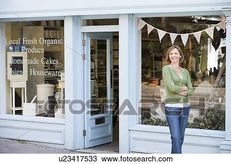 Stock Image - Woman standing in front of organic food store smiling. Fotosearch