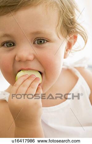 Stock Photograph - Baby indoors eating apple. Fotosearch