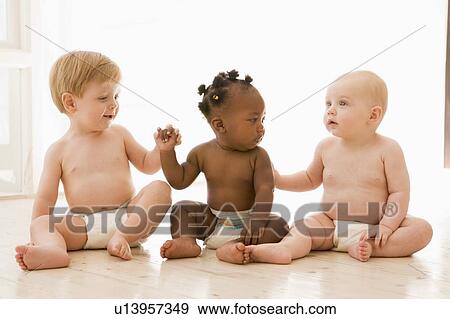 Stock Photo - Three babies sitting indoors holding hands. Fotosearch