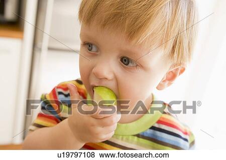 Stock Photo - Young boy eating apple indoors. Fotosearch