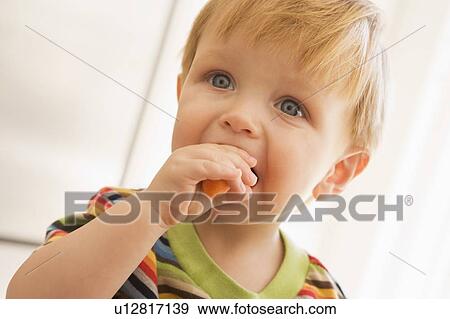 Stock Photo - Young boy eating carrot indoors. Fotosearch