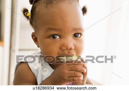Picture - Young girl eating apple indoors. Fotosearch