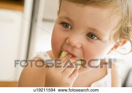 Picture - Young girl eating apple indoors. Fotosearch