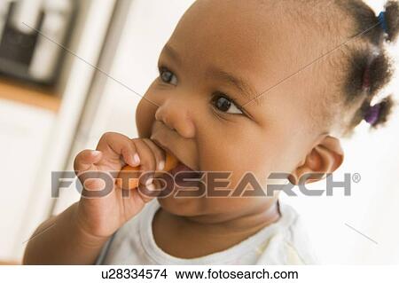 Picture - Young girl eating carrot indoors. Fotosearch