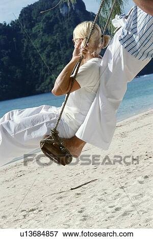 Stock Photo - Couple on a swing outdoors at the beach. Fotosearch