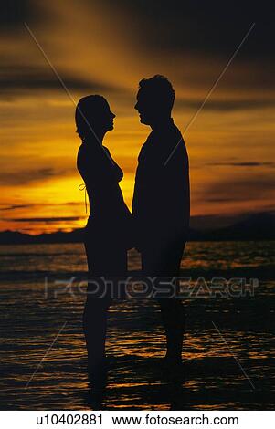 Couple standing on the beach holding hands at sunset (silhouette) View Large Photo Image Stock Image - Couple standing on the beach holding hands at sunset (silhouette). Fotosearch