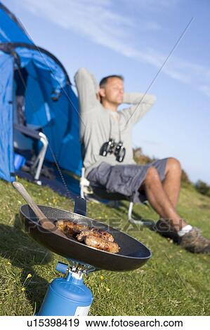 Stock Photo - Man camping outdoors and cooking. Fotosearch