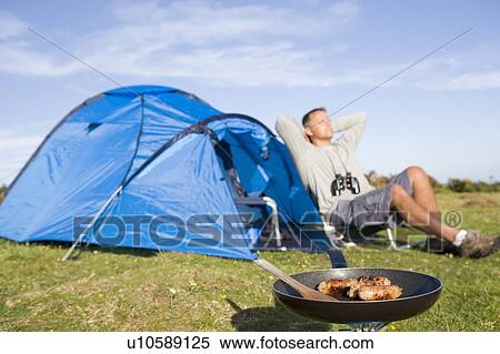 Stock Photography - Man camping outdoors and cooking. Fotosearch