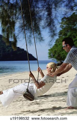 Man outdoors by a beach pushing a woman on a swing (selective focus) View Large Photo Image Stock Image - Man outdoors by a beach pushing a woman on a swing (selective focus). Fotosearch