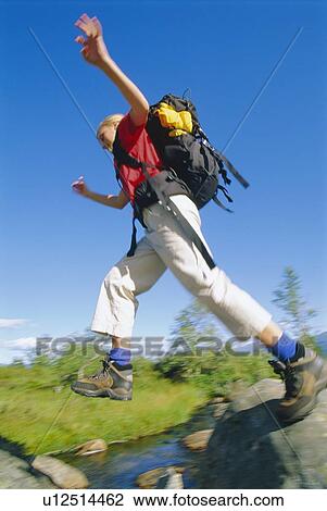 Stock Image - Woman hiking outdoors jumping over stream (blur). Fotosearch