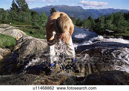 Stock Image - Woman outdoors by river splashing water on face (selective focus). Fotosearch