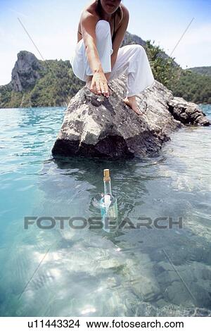 Woman outdoors reaching into ocean for bottle with note inside (selective focus) View Large Photo Image Picture - Woman outdoors reaching into ocean for bottle with note inside (selective focus). Fotosearch