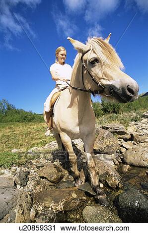 Stock Image - Woman outdoors riding horse through stream (fisheye). Fotosearch