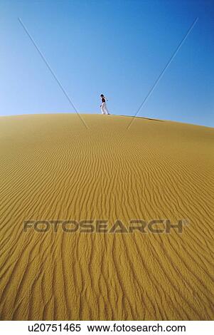 Stock Photography - Woman outdoors walking in the desert (far away). Fotosearch