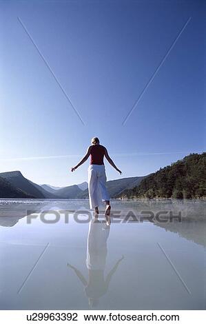 Stock Image - Woman outdoors walking on water in scenic location. Fotosearch
